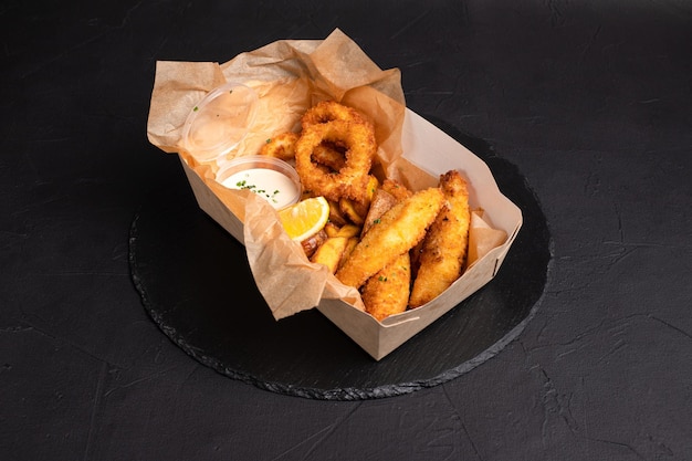 Beer snacks squid rings cheese sticks French fries on a black background side view