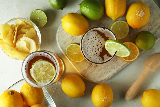 Beer with citrus on white textured table, top view