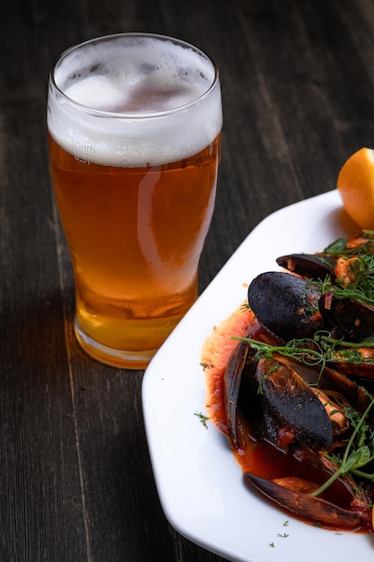 Beer with mussels in tomato sauce with microgreens and lemon on a wooden background