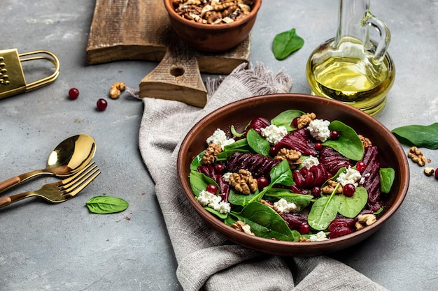 Beet or beetroot salad with baby spinach cheese nuts cranberries on plate with fork dressing and spices on gray background top view place for text