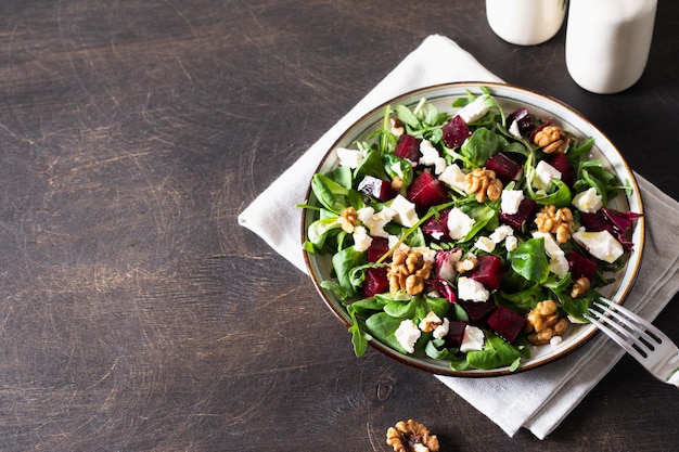 Beet or beetroot salad with fresh arugula soft cheese and walnuts on plate dressing and spices