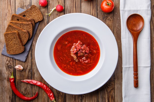 Beet soup in white plate with vegetables on wooden table. Borch, traditional Russian food