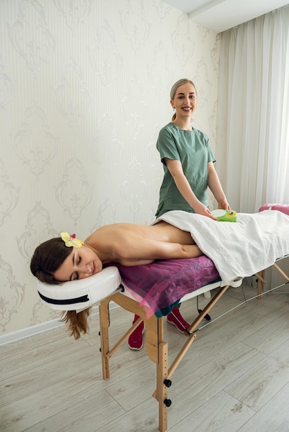 Before professional massage procedure female cosmetologist standing near her client