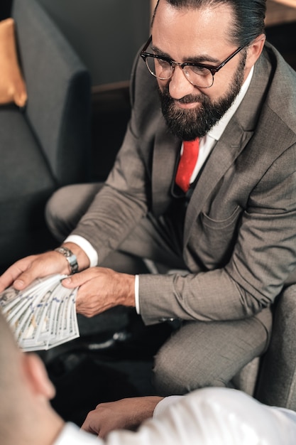 Behaving illegal. Bearded lawyer wearing glasses behaving illegal while receiving bribe from client