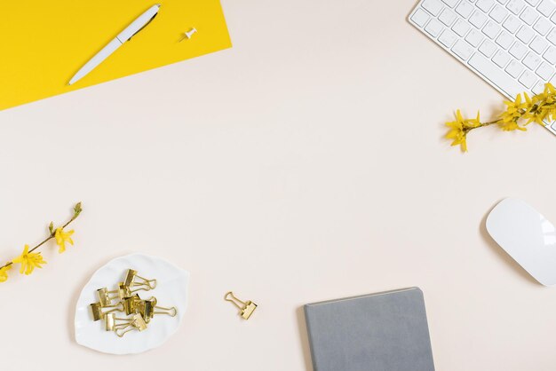 On a beige background flat lay with a yellow flower a notepad keyboard and paper clips a female floral desktop The concept of a stylish spring or summer morning Top view and copy space