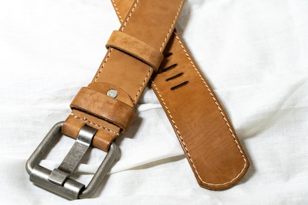 Beige belt made of thick genuine leather on a white background made of linen fabric Production of handmade belts from natural environmentally friendly materials