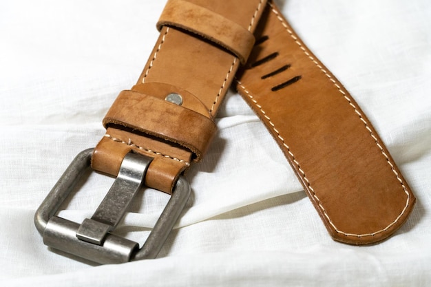 Beige belt made of thick genuine leather on a white background made of linen fabric Production of handmade belts from natural environmentally friendly materials