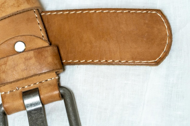 Beige belt made of thick genuine leather on a white background made of linen fabric Production of handmade belts from natural environmentally friendly materials