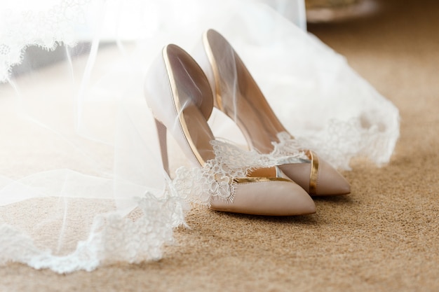 Beige bridal shoes standing on the floor, covered with a white veil with lace