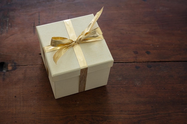 Beige closed gift box with gold color ribbon on wooden table