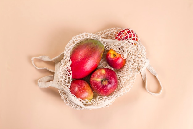 Beige mesh string bag with red fruits on a beige background.