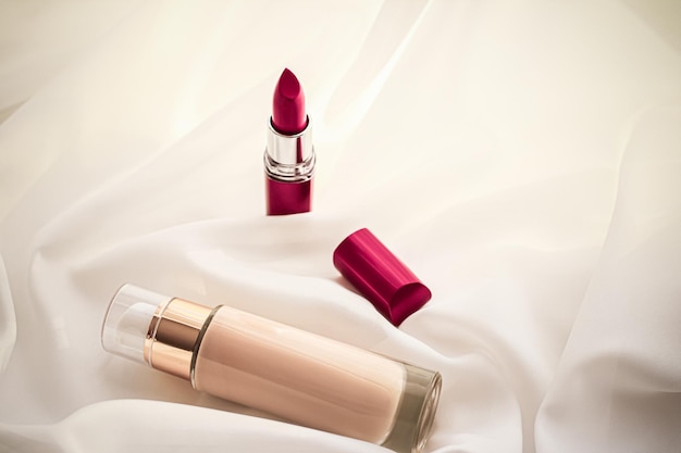 Beige tonal cream bottle makeup fluid foundation base and red lipstick on silk background cosmetics products as luxury beauty brand holiday design