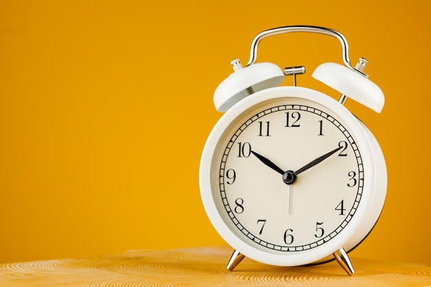 Beige vintage alarm clock on yellow background.