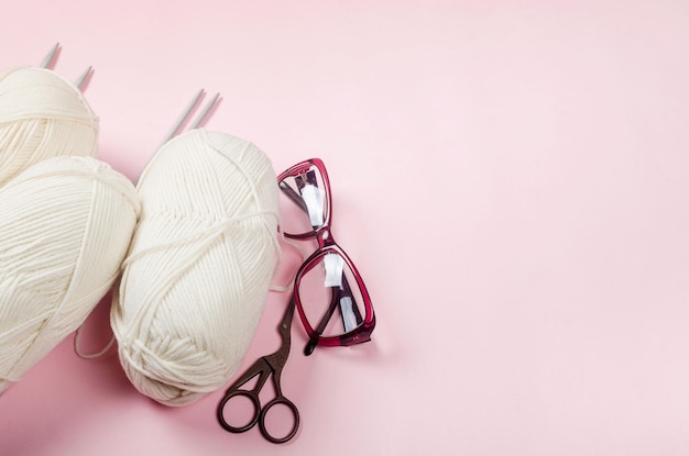 Beige yarn thread with knitting needles on a pink background for knitting