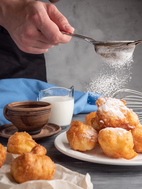 Beignet sprinkled with icing sugar on a wooden table with coffee and milk.