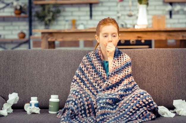 Photo being ill. unhappy sick girl being covered with plaid while suffering from an illness