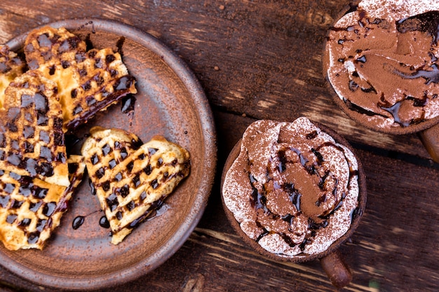 Belgian heart shaped waffle on brown plate with hot chocolate with marshmallow on wooden .