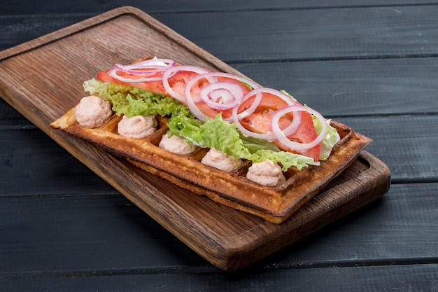 Belgian waffle with salmon cream tomatoes and salad On a dark wooden background