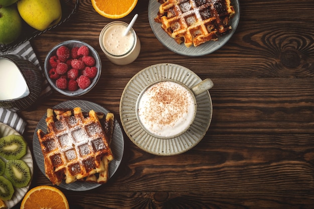 Belgian waffles, coffee, yogurt, fruits and berries on a wooden background, breakfast concept.