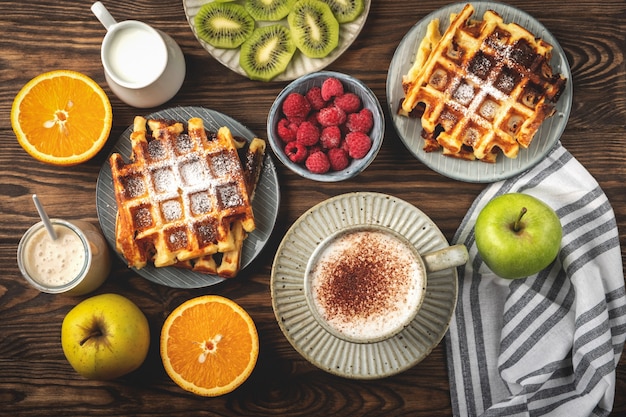 Belgian waffles, coffee, yogurt, fruits and berries on a wooden background, breakfast concept.