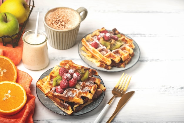 Belgian waffles, coffee, yogurt, fruits on a white wooden background, breakfast concept.