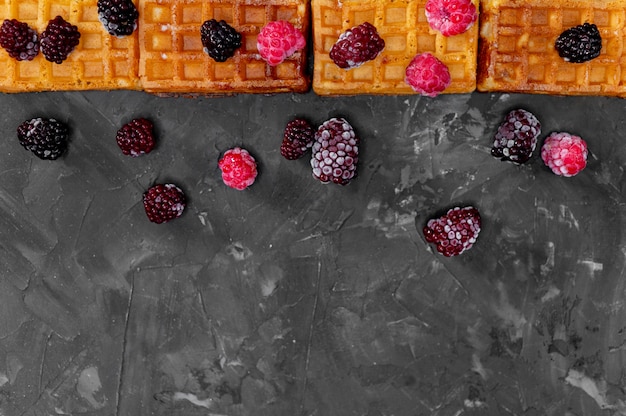 Belgian waffles with blackberries and raspberries on a gray background