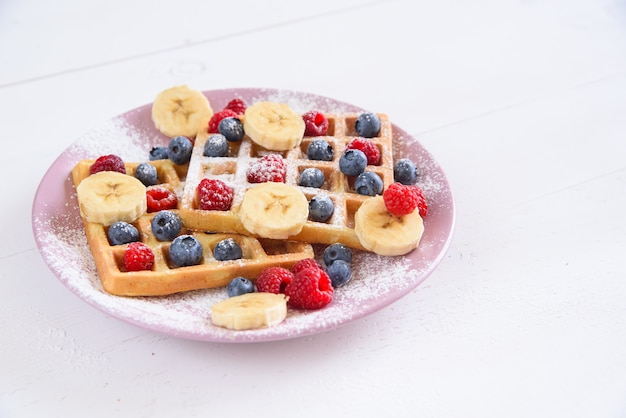 Belgian waffles with blueberries, raspberries, bananas and sugar powder . Concept of tasty and healthy food.