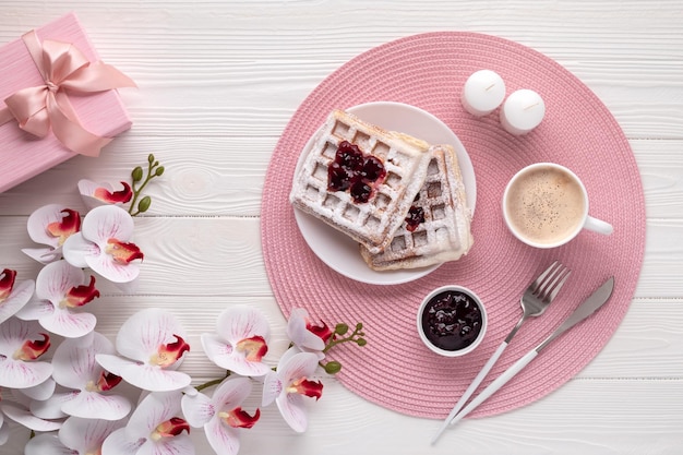 Belgian waffles with latte and orchid flower on white wooden table Top view Mother's day greeting card Food and drink background Coffee dessert on breakfast in morning Festive bouquet Lifestyle