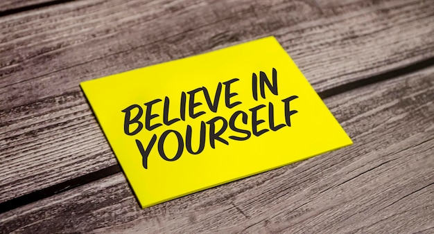 Believe in yourself concept Yellow paper and wooden background