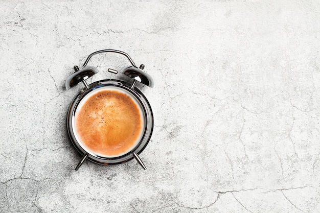 Bell alarm clock with a cup of coffe in clock face on a marble background with copy space