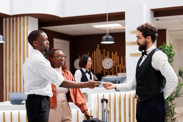 Bellboy accepting cash from hotel guest in reception lobby, offering luxury services to carry luggage at front desk. Young man giving tip to hotel concierge, helping with suitcases.