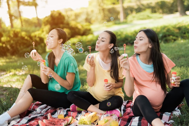 Belly women are blowing bubbles in park.