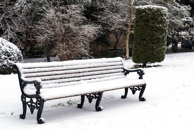 Bench in city park is covered with snow