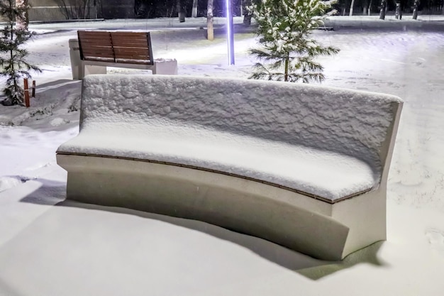 Bench in the snow in the city park at night in winter