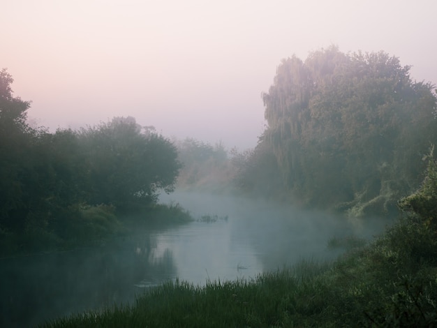 Bend of a small river in heavy fog at dawn