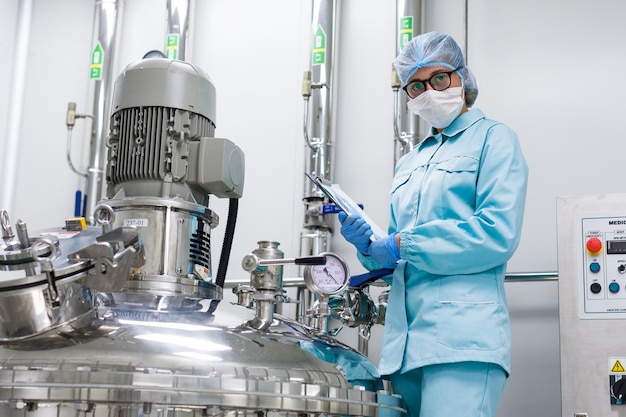 Bended scientist in blue lab uniform stand near compressors engine tablet in hands look at camera