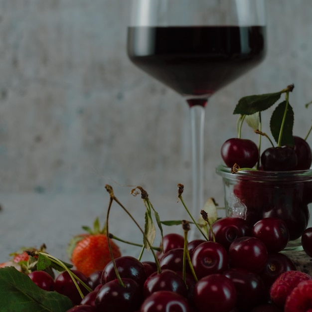 Berries grapes and strawberries on a gray concrete background Glass of red wine Copy space