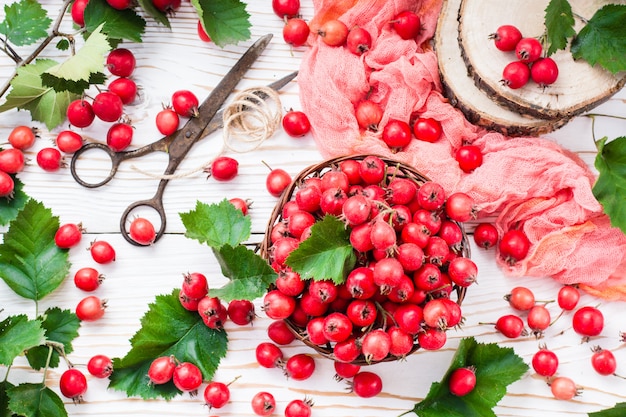 Berries and leaves of hawthorn in a wicker basket on a wooden table, top view