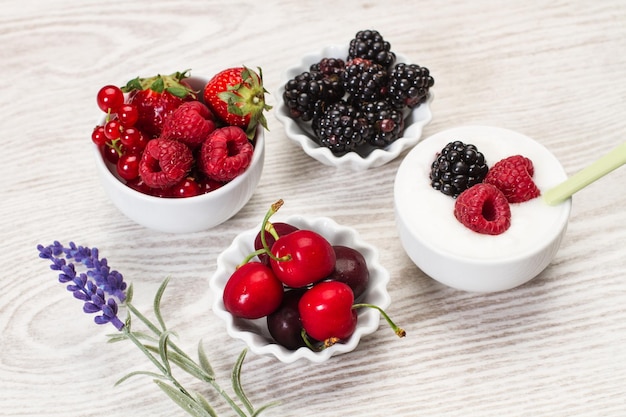 Berries in white bowls on a white wooden table in a top view