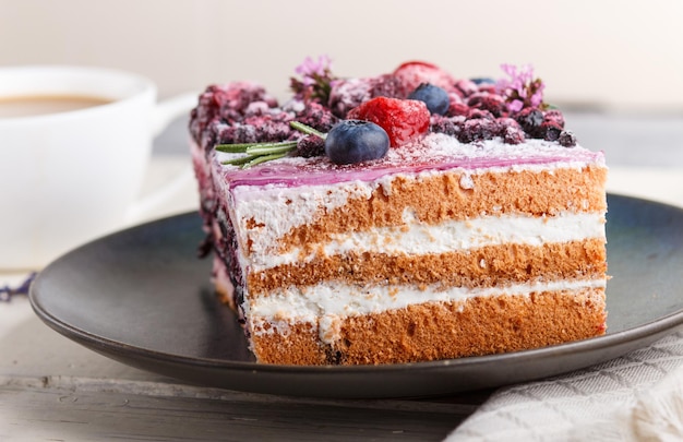 Berry cake with milk cream and blueberry jam on blue ceramic plate with cup of coffee and fresh blueberries on a white wooden background. side view, close up, selective focus.