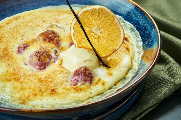 Berry gratin with ice cream in a blue bowl on wooden table. Tasty and sweet french baked dessert. Close up, selective focus