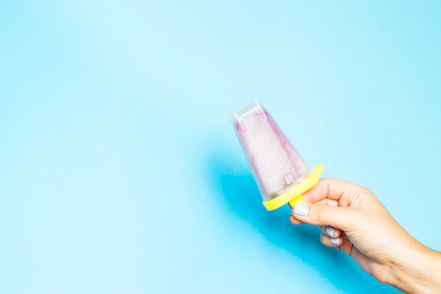 Berry homemade ice cream in plastic form in a female hand on a blue background