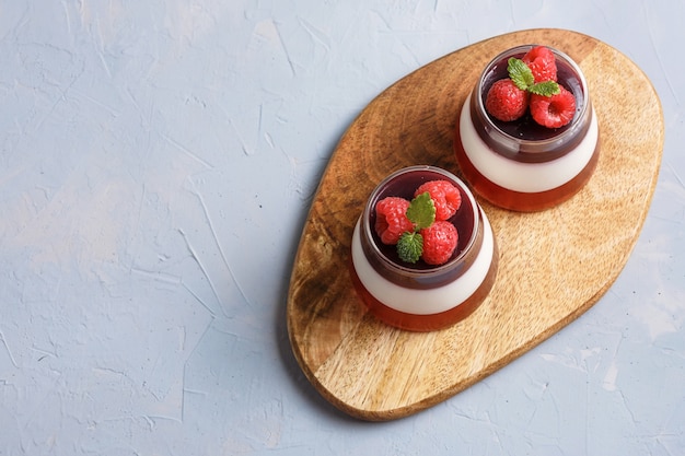 Berry jelly topping with raspberries in a glass cup on a wood stand