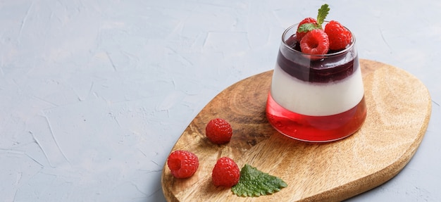 Berry jelly topping with raspberries in a glass cup on a wood stand