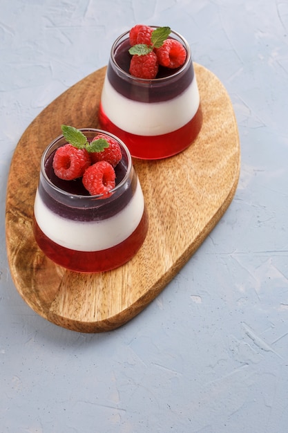 Berry jelly topping with raspberries in a glass cup on a wood stand