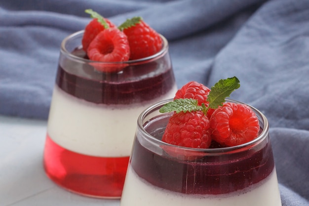 Berry jelly with raspberries in a glass cup on light blue background. Blue textile on the table.