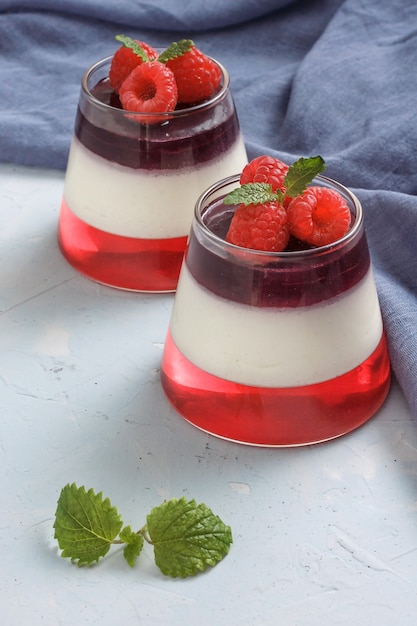 Berry jelly with raspberries in a glass cup on light blue background. Blue textile on the table.