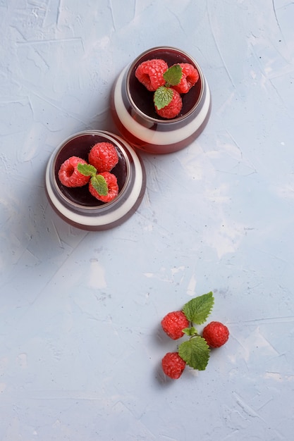 Berry jelly with raspberries in a glass cup on light blue background.