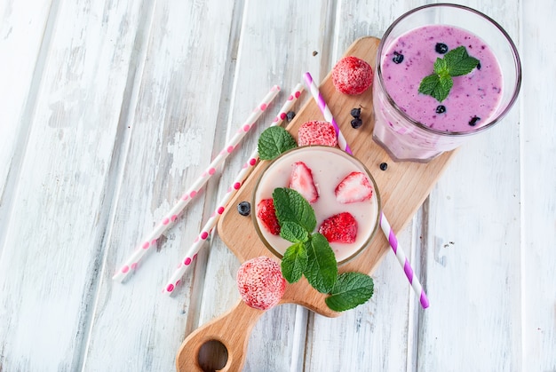 Berry smoothies of strawberries, banana and blueberries in glasses and ingredients on a wooden table