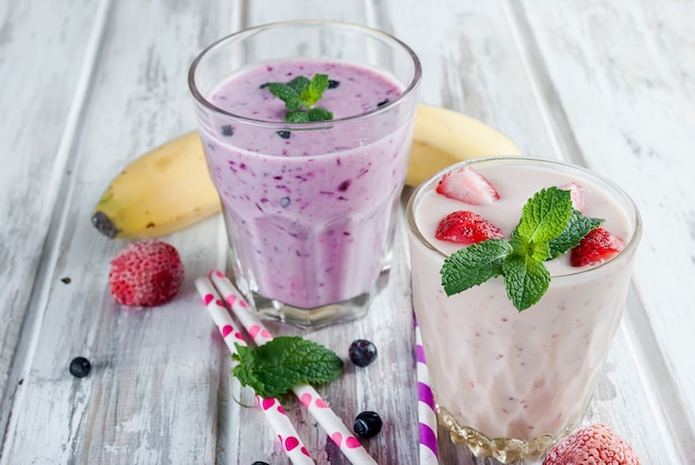 Berry smoothies of strawberries, banana and blueberries in glasses and ingredients 